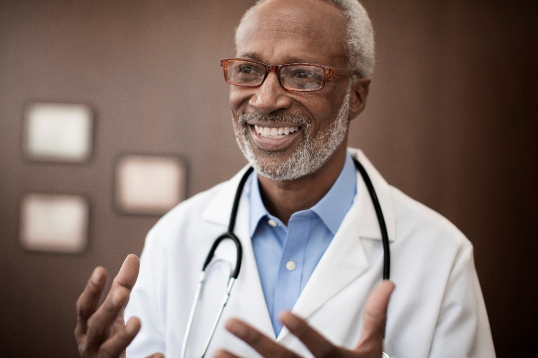 Man with white coat and stethoscope smiling. 
